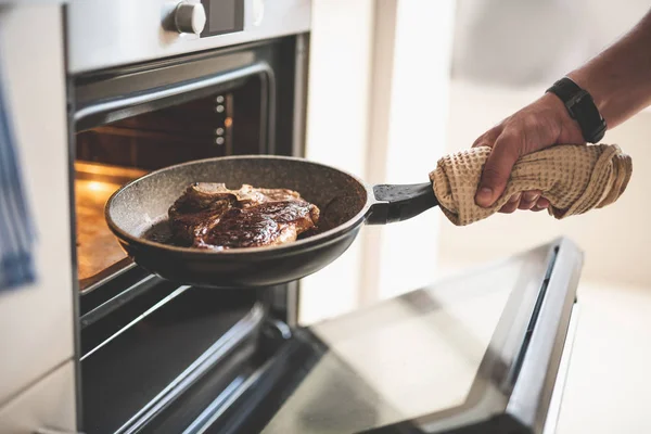 Ο άνθρωπος βάζοντας κρέας στο φούρνο, ενώ το μαγείρεμα το δείπνο — Φωτογραφία Αρχείου