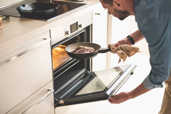 Hombre barbudo poniendo carne en el horno mientras cocina la cena — Foto de Stock