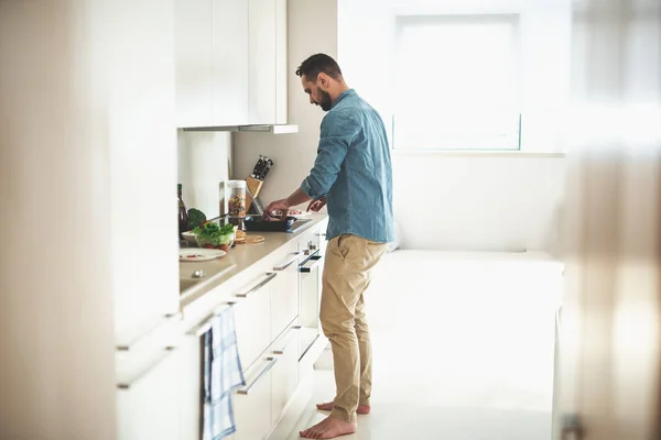 Joven barbudo hombre cocina cena en acogedora cocina — Foto de Stock