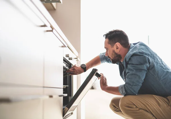 Ung bearded man kontrollera beredskap maträtt på ugn — Stockfoto