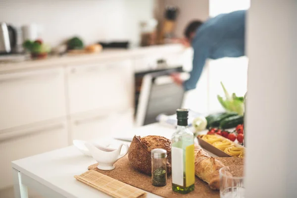 Table with ingredients for cooking and young man on blurred background — Stock Photo, Image