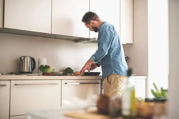 Bearded man holding burger bun while standing in kitchen — Stock Photo, Image