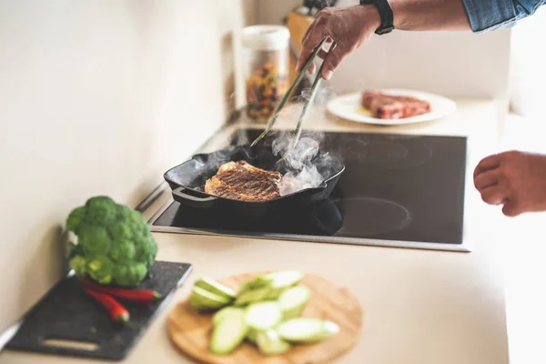 Homem segurando pinças enquanto cozinha delicioso bife de carne na cozinha — Fotografia de Stock