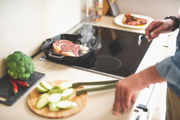 Pedaço de carne com vapor fritando em fogão enquanto o homem segurando garfo — Fotografia de Stock