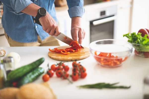 Hombre preparando ingredientes para ensalada de verduras mientras está de pie cerca de la mesa de la cocina — Foto de Stock