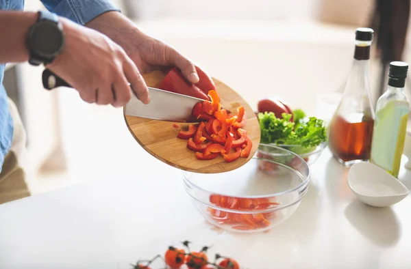 Hombre poniendo rodajas de pimiento rojo al tazón mientras cocina la cena — Foto de Stock