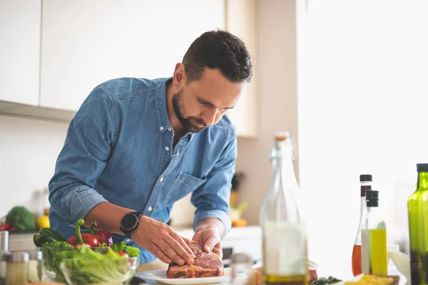 Jonge man koken van vlees terwijl je in de buurt van keukentafel met baard — Stockfoto