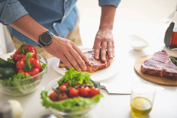 Man voorbereiding van rauw vlees voor het koken terwijl je in de buurt van keukentafel — Stockfoto