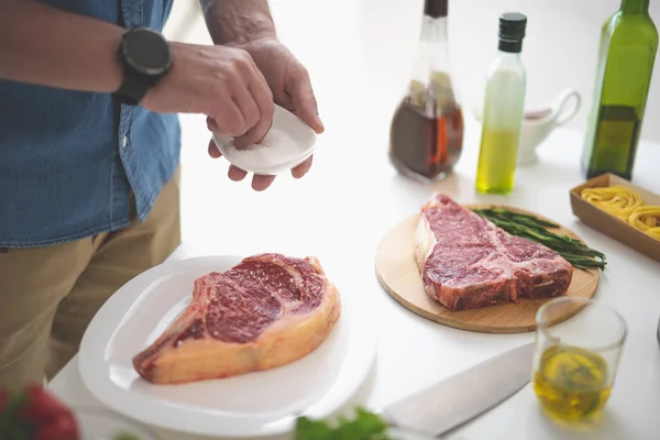 Mann kocht Fleisch, während er am weißen Küchentisch steht — Stockfoto