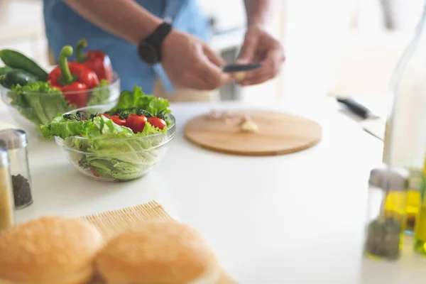 Hombre preparando ajo mientras los ingredientes para ensalada esperan en la mesa — Foto de Stock