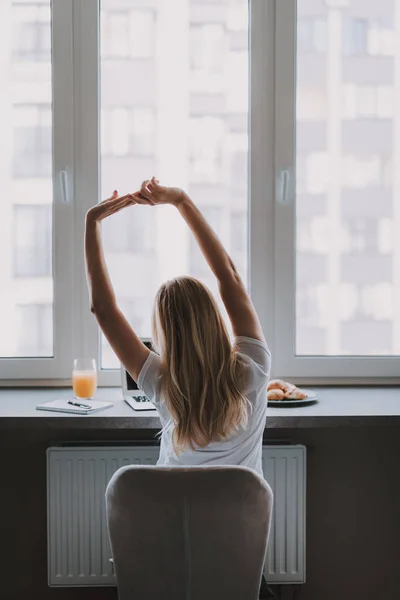 Blonde girl sitting at computer and stretching