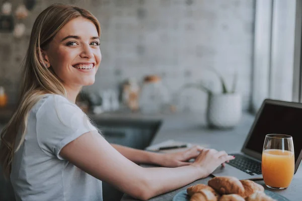 Freelancer loira bonita sentado com laptop, suco e donuts em casa — Fotografia de Stock