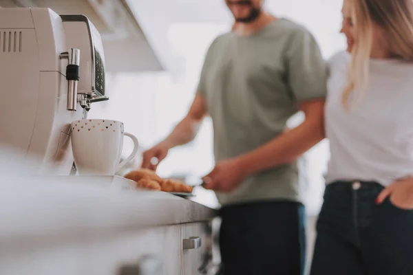 White cup near coffee machine with young happy couple on background — Stock Photo, Image