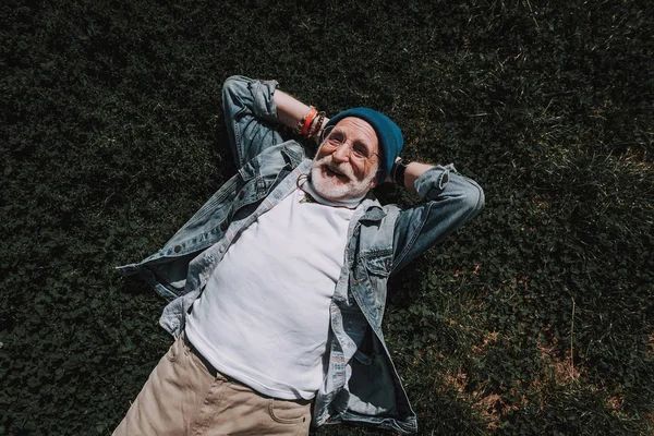 流行に敏感な老人の笑顔は草に横たわっています。 — ストック写真