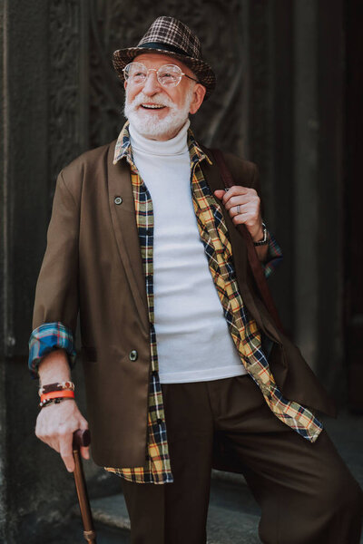 Cheerful pensioner staying on steps of grand building and smiling