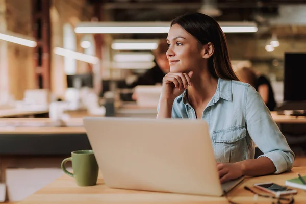 Aantrekkelijke jonge vrouw zittend aan tafel met laptop en kopje koffie — Stockfoto