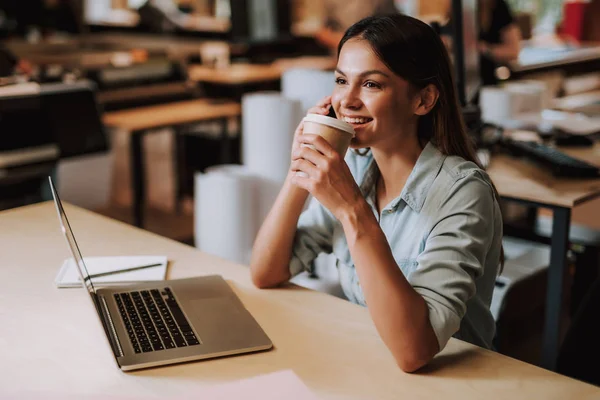 Härlig ung kvinna talar på mobiltelefon och njuter av kaffe på jobbet — Stockfoto