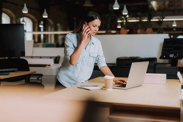 Bella signorina che parla sul cellulare mentre guarda il computer portatile — Foto Stock