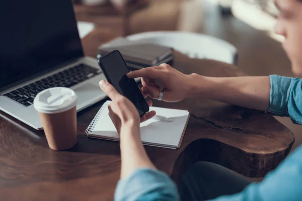 Young person touching the screen of smartphone while sitting at the table — Stock Photo, Image