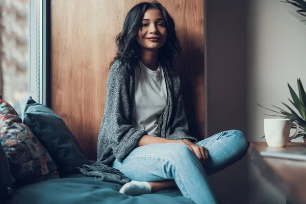 Cintura para cima de senhora bonita sentado no peitoril da janela confortável e sorrindo — Fotografia de Stock