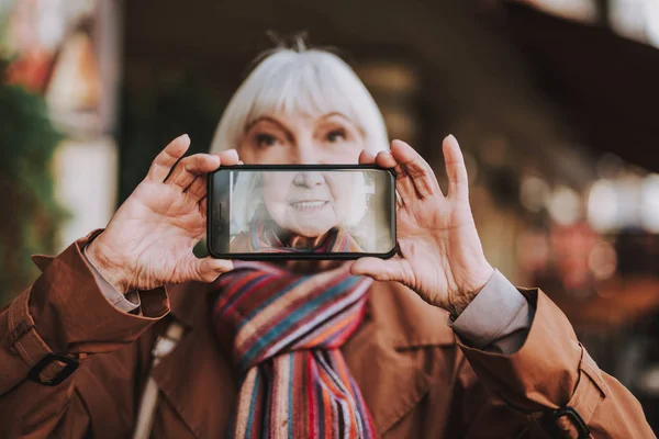 Радостная пожилая леди делает селфи на улице — стоковое фото