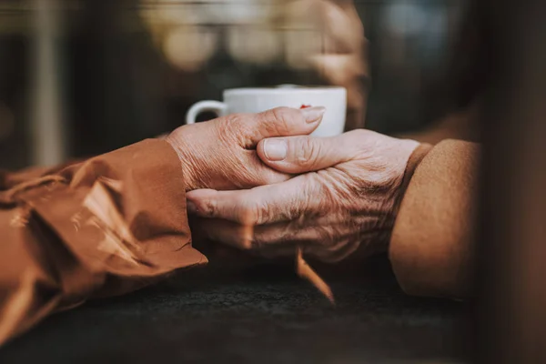 Bejaarde echtpaar hand in hand met warme dranken op onscherpe achtergrond — Stockfoto