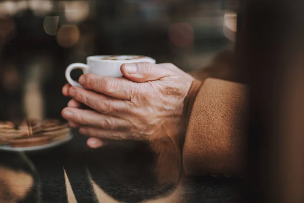 Old gentleman holding hot drink on blurred background