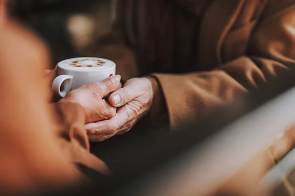 Idősebb pár tartja kezében cappuccinóval, miközben az asztalnál ül — Stock Fotó