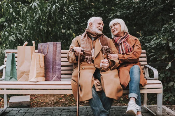 Счастливая пожилая пара сидит на скамейке с пакетами для покупок — стоковое фото