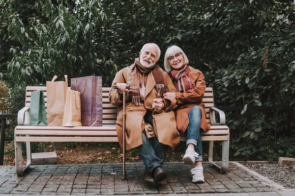 Schönes älteres Paar sitzt mit Einkaufstüten auf Bank — Stockfoto
