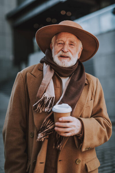 Stylish old man with hot drink standing on the street
