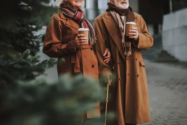 Feliz pareja de ancianos con bebidas calientes caminando por la calle — Foto de Stock