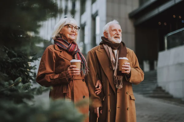 Hermosa pareja de ancianos con bebidas calientes caminando por la calle —  Fotos de Stock