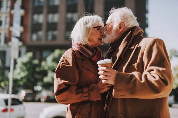 Schönes älteres Paar mit heißen Getränken, die ihre Liebe auf der Straße ausdrücken — Stockfoto