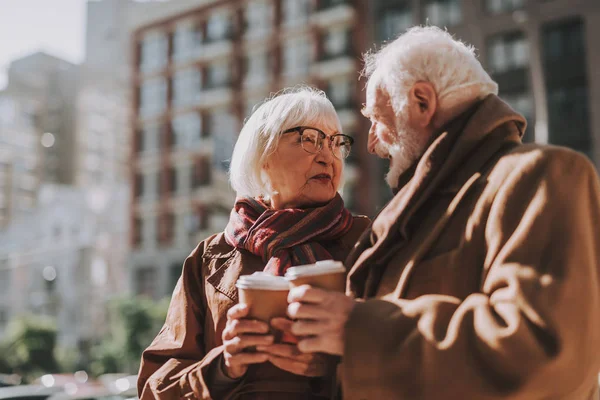 Hermosa pareja de ancianos con bebidas calientes mirándose y sonriendo — Foto de Stock