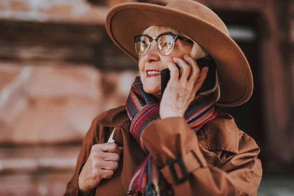 Стильна стара жінка в капелюсі говорить на мобільному телефоні на вулиці — стокове фото