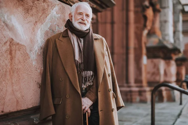 Stylish senior gentleman with cane posing near old building