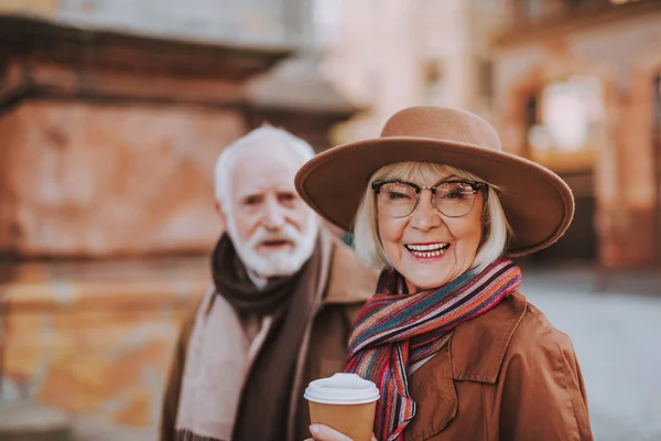 Fröhliche Seniorin mit Kaffee und bärtigem Mann auf verschwommenem Hintergrund — Stockfoto