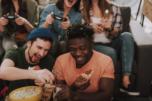 Two male friends clinking bottles of beer while girls playing video games — Stock Photo, Image