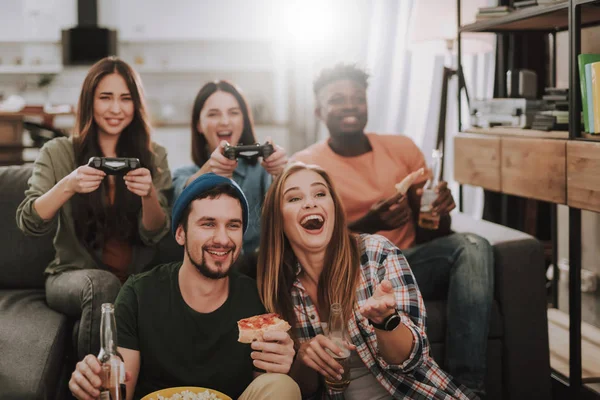 Jóvenes alegres jugando videojuegos mientras disfrutan de bebidas y comida —  Fotos de Stock