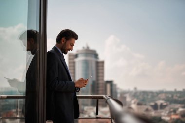 Bir duraklama almak. Bel kadar masaj Smartphone cep telefonu ile office teras üzerinde dururken okuma gülümseyen işadamı portresi. Kopya alanı sağ