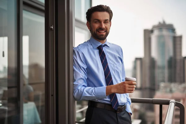 Corporate time-out culture. Waist up portrait of smiling businessman standing on office balcony with cup of coffee while having break