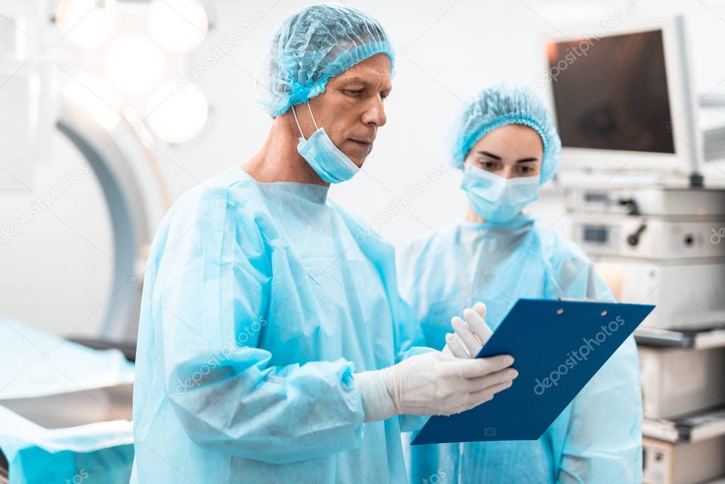 Calm doctor holding blue clipboard and talking to colleague