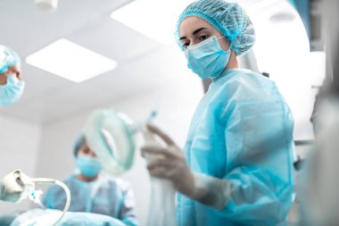 Tıbbi işçi işlem odasında dururken oksijen maskesi bakarak