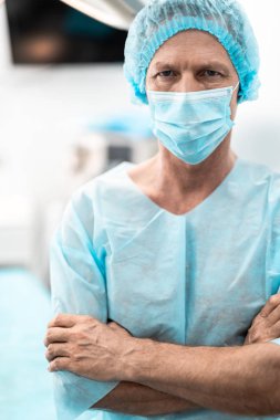 Ameliyat odasında duran çapraz kolları olan orta yaşlı Doktor