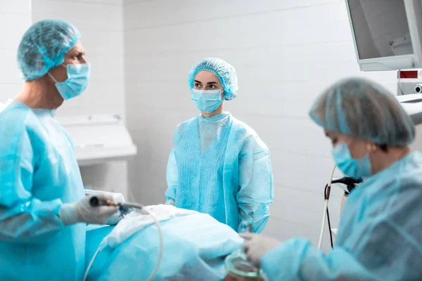 Enfermera joven en máscara protectora mirando al cirujano durante la operación quirúrgica — Foto de Stock