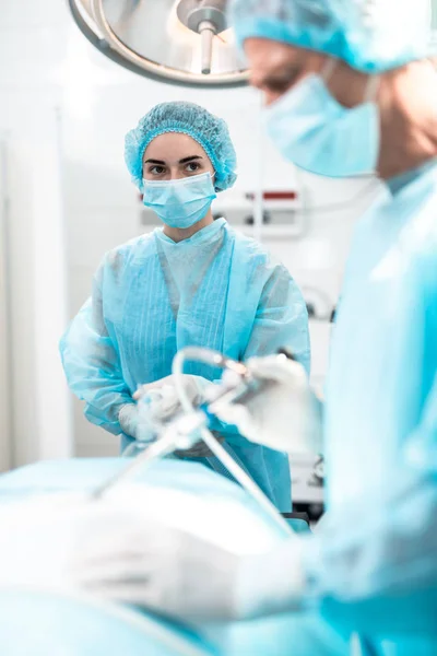 Медсестра в синем платье держит кислородную маску на лице пациента во время операции — стоковое фото