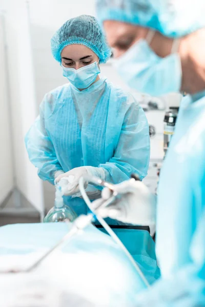 Jovem enfermeira segurando máscara de oxigênio no rosto do paciente durante a operação cirúrgica — Fotografia de Stock