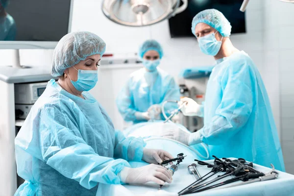 Enfermeira tomando instrumento laparoscópico enquanto médico realizando cirurgia — Fotografia de Stock