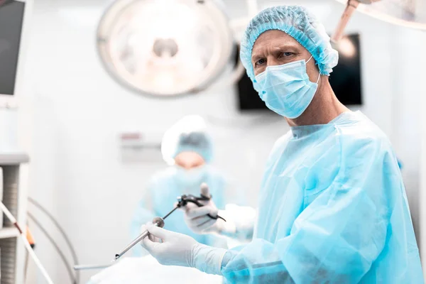 Хирург с лапароскопическим инструментом, стоящим в операционной — стоковое фото